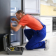 Male-Technician-With-Screwdriver-Repairing-Refrigerator-in-Kitchen